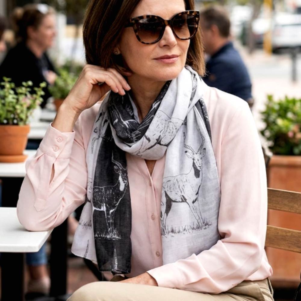 Woman wearing a light pink blouse and a patterned antelope print scarf outdoors.