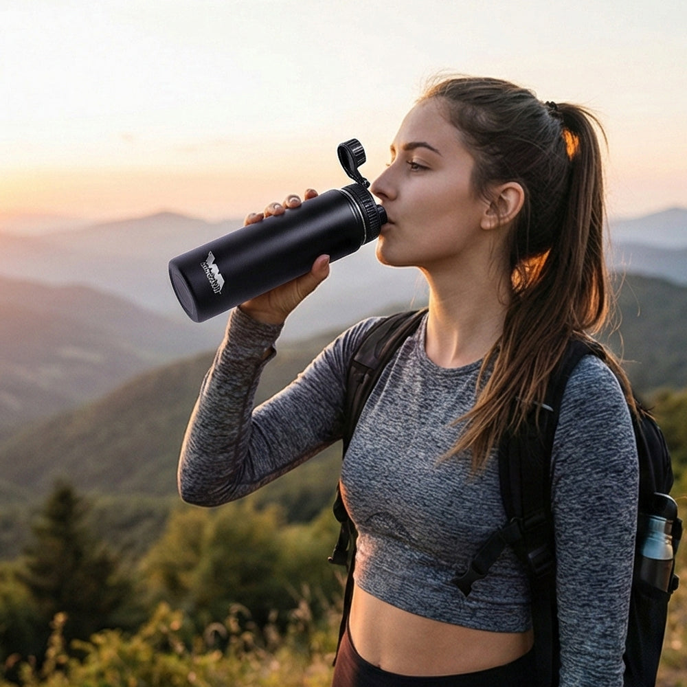 Woman drinking from a black water bottle with mountains in the background